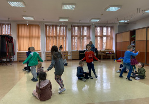 Dzieci tańczą w parach na zajęciach. Jedno dziecko kuca, drugie kręci się wokół niego